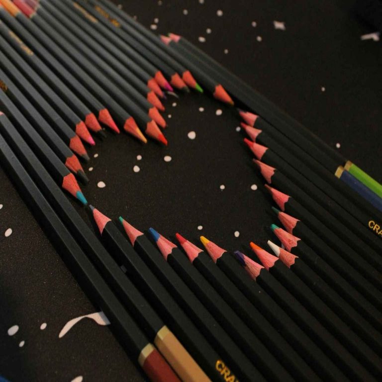 Lápices de colores formando un corazón sobre fondo oscuro, símbolo de creatividad y emoción
